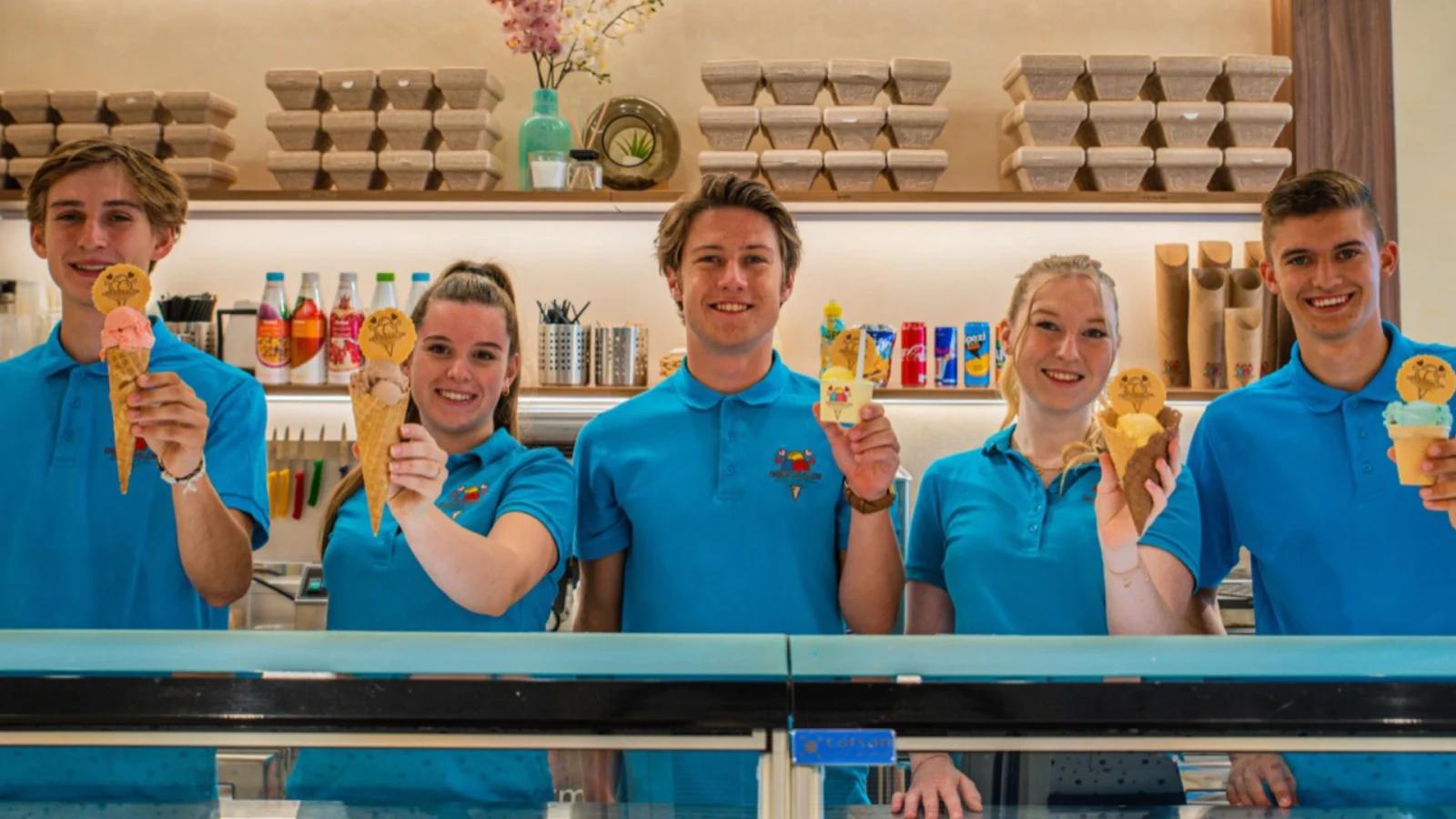 Team von Der Eissalon in Graz in blauen Polos hinter der Theke, jede und jeder mit einer Eistüte in der Hand
