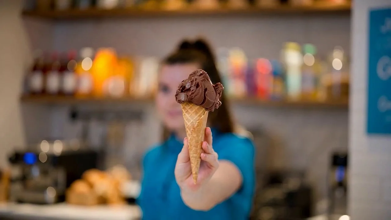 Mitarbeiterin von Der Eissalon in Graz hält eine Waffeltüte mit Schokoladeneis in die Kamera